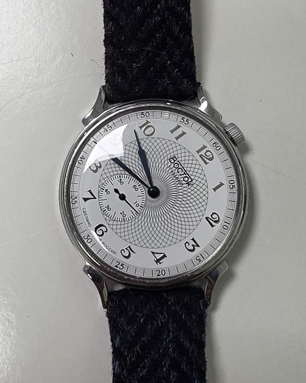Vostok 581096 Prestige on a dark herringbone tweed strap, showing the tilted white dial with a guilloché centre and small seconds